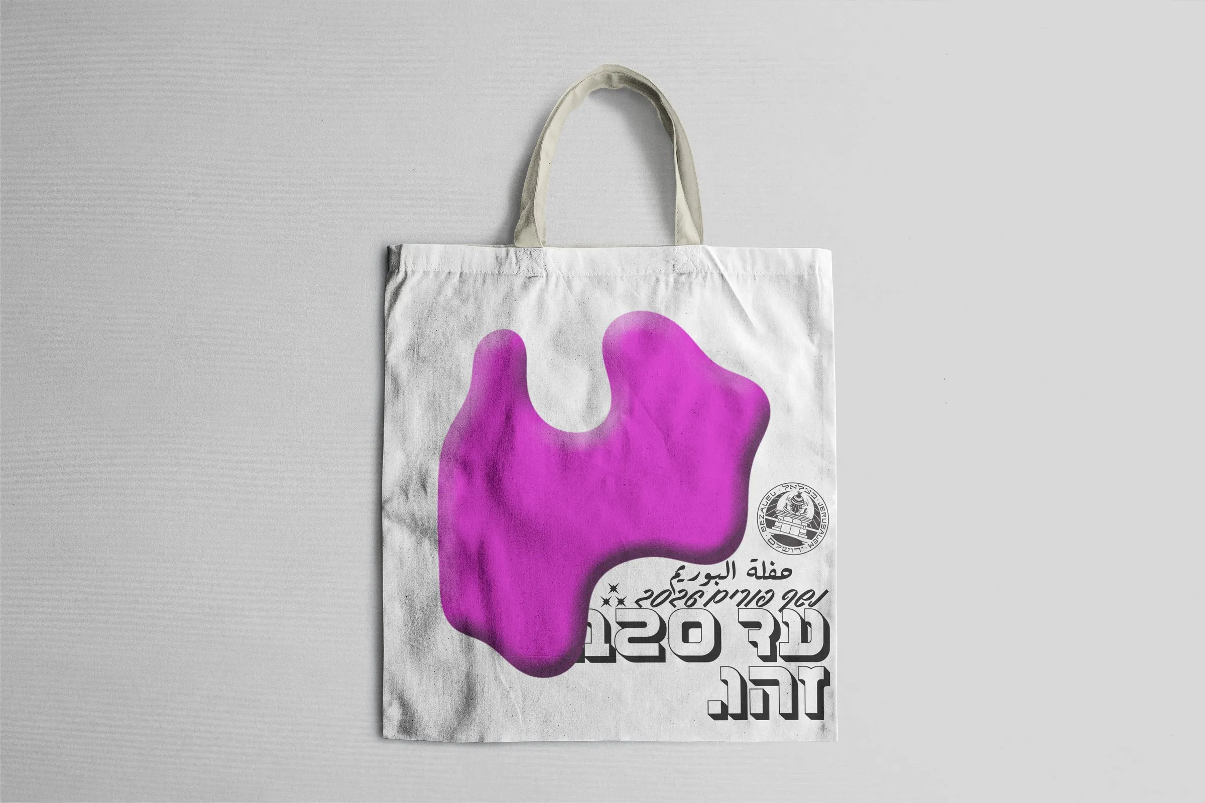 A tote bag with the magenta blob and the Purim ball logotype