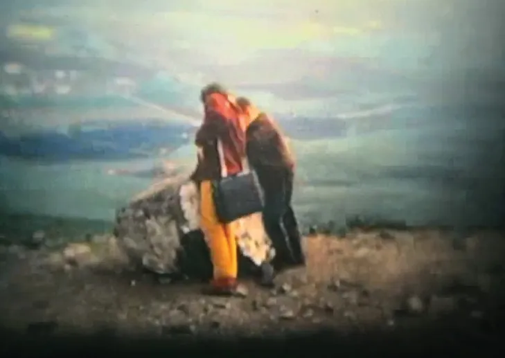 A couple embracing on a rocky hilltop above a valley