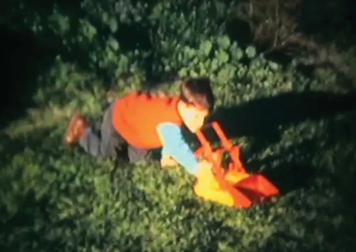 A child in an orange sweater crawling on the grass beside a toy