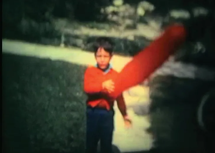 A boy in a red sweater on a lawn, a streak of red light across the frame