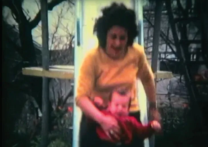 A woman in a yellow sweater laughing as she lifts a baby